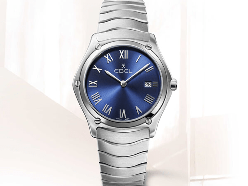 Juwelier-Wagner-Madler-Uhren-Ebel-Sport-Ansicht Eine elegante Edelstahluhr mit metallisch blauem Zifferblatt und 12 römischen Stundenmarkierungen. Die Marke „Ebel“ ist auf dem Zifferblatt deutlich zu erkennen, außerdem gibt es auf der 3-Uhr-Position eine Datumsanzeige. Das Armband besteht aus einer Reihe horizontaler Glieder.