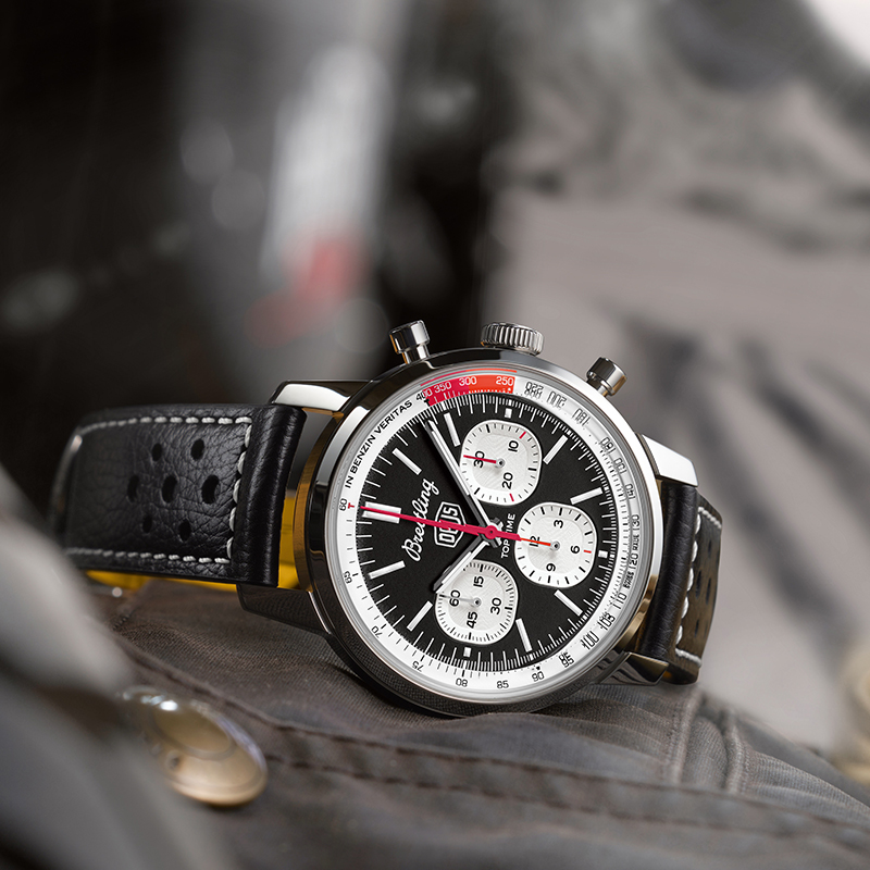 Juwelier-Wagner-Madler-Breitling-Kollektionen-Top-Time-Vorschau Eine Nahaufnahme einer luxuriösen Breitling-Armbanduhr mit schwarzem Lederarmband. Die Uhr verfügt über ein detailliertes schwarzes Zifferblatt mit drei kleineren Zifferblättern, einem Tachymeter am äußeren Rand und dem deutlich sichtbaren Markenlogo und -namen. Der Hintergrund ist unscharf und hebt die Uhr hervor.