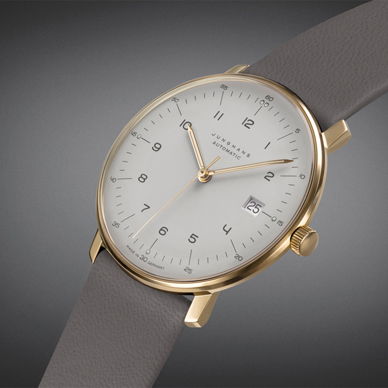 Juwelier-Wagner-Madler-Junghans-Kollektionen-Vorschau Eine stilvolle Junghans-Armbanduhr mit goldenem Gehäuse, weißem Zifferblatt und grauem Lederarmband. Das Zifferblatt verfügt über minimalistische Zahlen, goldene Zeiger und ein kleines Datumsfenster mit „25“. Der Markenname „Junghans“ und „Automatic“ sind auf dem Zifferblatt aufgedruckt.