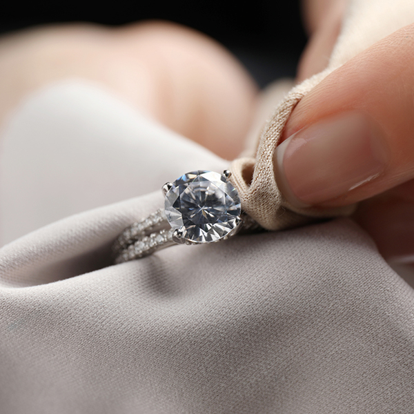 Nahaufnahme einer Hand, die einen funkelnden Diamantring hält und mit einem Tuch poliert. Der in einer renommierten Schmuckwerkstatt gefertigte Ring verfügt über einen markanten Diamanten im Rundschliff und ein Band, das mit kleineren Diamanten verziert ist, alles in glänzendes Metall eingefasst.