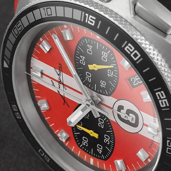 Juwelier-Wagner-Madler-Uhren-Junghans-Kollektion-1972-ansicht-3 Nahaufnahme einer Armbanduhr aus der Junghans 1972 Kollektion mit rot-weißem Zifferblatt, schwarzen Hilfszifferblättern, silbernen Zeigern und gelben Akzenten. Die Metalllünette mit markierten Zahlen ergänzt die silberne Krone. Der schlanke silberne Sekundenzeiger kontrastiert mit den breiten und markanten Hauptzeigern.