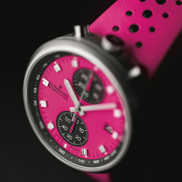 Juwelier-Wagner-Madler-Uhren-Junghans-Kollektion-1972-ansicht Nahaufnahme einer rosa Sportarmbanduhr aus der Junghans 1972 Kollektion mit einem schwarz-weißen Dual-Chronographen-Zifferblatt. Das Armband ist ebenfalls rosa mit schwarzen Perforationen. Das Zifferblatt zeigt Markierungen und Zahlen für die Zeitmessung und Stoppuhrfunktionen.