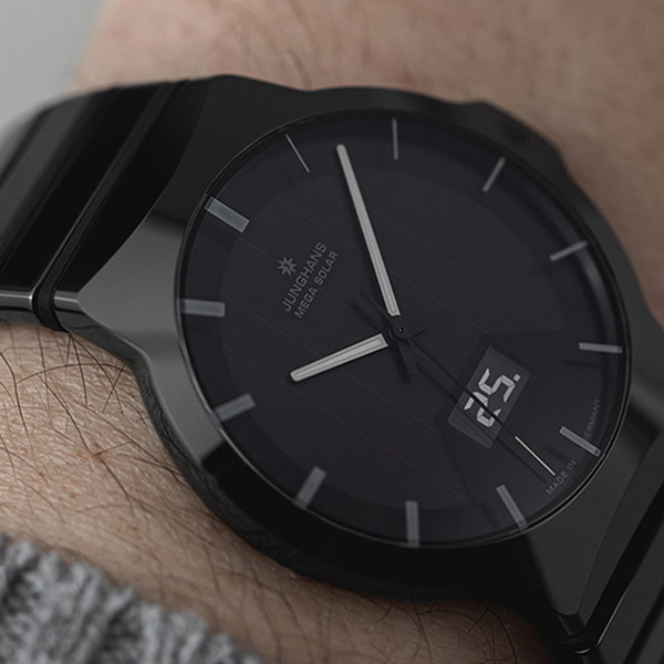 Juwelier-Wagner-Madler-Uhren-Junghans-Kollektion-force-ansicht Nahaufnahme eines Handgelenks mit einer schwarzen Junghans Mega Solar-Uhr aus der Force Kollektion. Die Uhr hat ein schlankes, dunkles Zifferblatt mit silbernen Zeigern, minimalistisches Design und eine eingelassene Datumsanzeige mit der Zahl 25. Das Handgelenk ist teilweise von einem grauen Pulloverbündchen bedeckt.