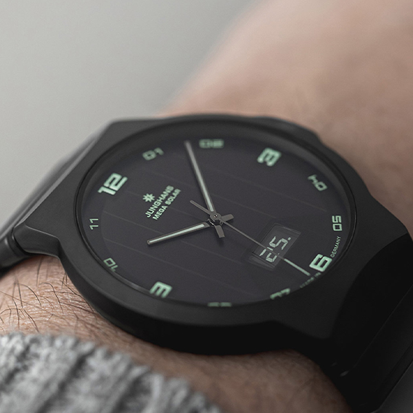 Juwelier-Wagner-Madler-Uhren-Junghans-Kollektion-force-ansicht-3 Eine Nahaufnahme einer Armbanduhr am Handgelenk einer Person. Die Uhr, die denen der Junghans Force Kollektion ähnelt, verfügt über ein schwarzes Armband und Gehäuse mit leuchtend grünen Ziffern und Zeigern. Das Zifferblatt zeigt die Marke „SIS“ und zeigt die Zeit als ungefähr 10:07 Uhr an, mit einem kleinen Datumsfenster unten.