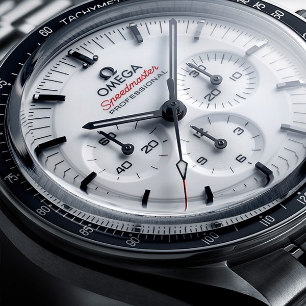 OMEGA © 2024 Nahaufnahme einer Omega Speedmaster Professional-Armbanduhr aus der Omega Speedmaster Kollektion mit weißem Zifferblatt mit schwarzen Details. Das Zifferblatt umfasst drei Hilfszifferblätter, kräftige schwarze Stundenmarkierungen und ein rotes Speedmaster-Logo. Die äußere Lünette ist schwarz mit einer Tachymeterskala und die Zeiger sind präzise und glatt.
