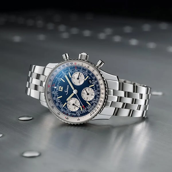 Juwelier-Wagner-Madler-Uhren-Sinn-Kollektionen-Chronographen Eine Edelstahlarmbanduhr aus der Sinn Instrumentelle Chronographen Kollektion mit poliertem Metallarmband und blauem Zifferblatt mit mehreren Hilfszifferblättern und aufwendigen Markierungen auf einer metallischen Oberfläche. Diese Uhr besticht durch ein sportliches und doch anspruchsvolles Design mit einer detaillierten Lünette und markanten Drückern.