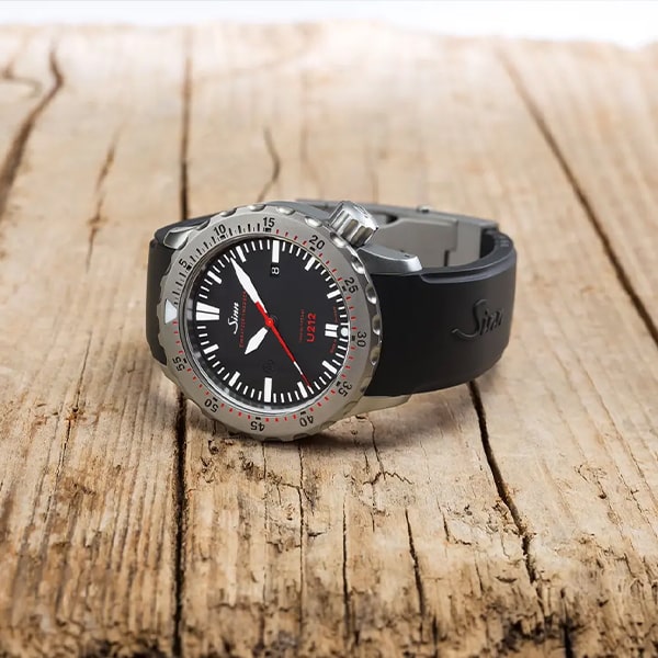 Eine schwarze Armbanduhr aus der Sinn instrumentelle Uhren Kollektion mit rundem Zifferblatt mit weißen und roten Markierungen, schwarzem Armband und silberner Lünette ruht auf einer rustikalen Holzoberfläche. Die Uhrzeiger und Stundenmarkierungen sind auf dem schwarzen Zifferblatt gut sichtbar.