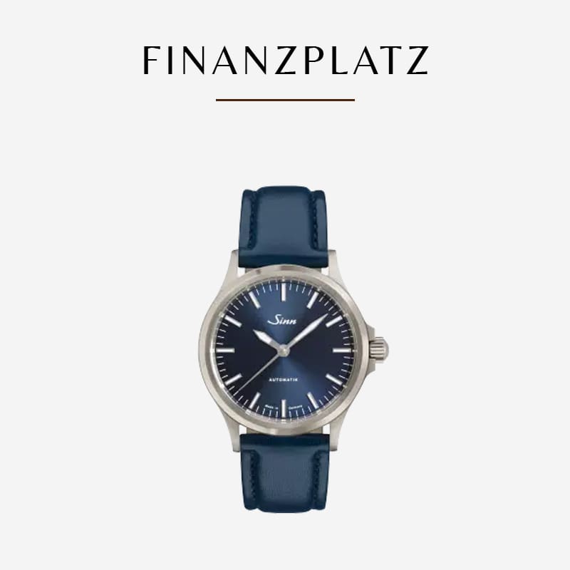 Eine Armbanduhr mit blauem Lederarmband und marineblauem Zifferblatt, auf dem der Markenname „Sinn“ und „Automatic“ stehen. Die Uhr steht auf einem schlichten weißen Hintergrund, darüber steht in fetten Großbuchstaben das Wort „FINANZPLATZ“.
