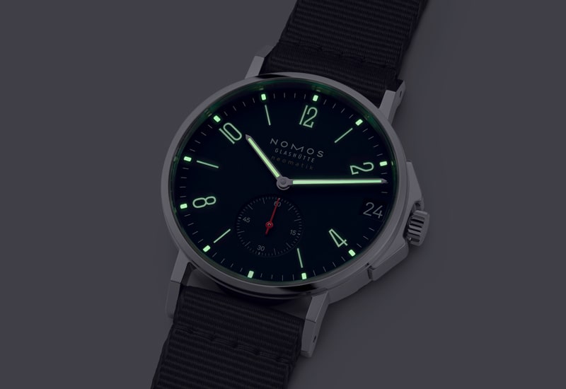 Juwelier-Wagner-Madler-Uhren-Nomos-Glashuette-Ahoi-Kollektion-Ansicht-2 Eine Armbanduhr aus der Nomos Ahoi Kollektion verfügt über ein dunkles Zifferblatt mit leuchtend grünen Ziffern. Die Zeiger und Stundenmarkierungen sind beleuchtet, ergänzt durch ein schwarzes Armband und ein kleines Hilfszifferblatt. Der prestigeträchtige Markenname „Nomos Glashütte“ ziert das Zifferblatt.