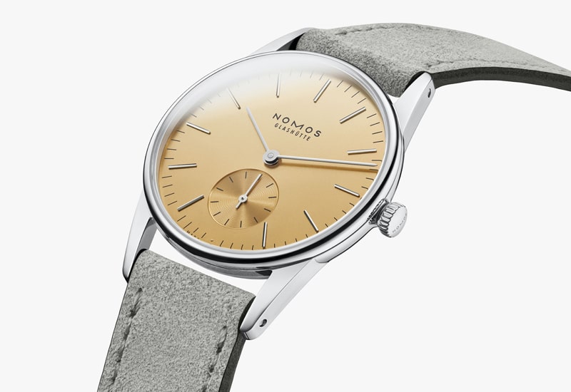 Juwelier-Wagner-Madler-Uhren-Nomos-Glashuette-Orion-Kollektion-Ansicht-3 Diese Armbanduhr aus der Nomos Orion Kollektion besticht durch ein minimalistisches Design mit beigem Zifferblatt, silbernen Markierungen und einem kleinen Hilfszifferblatt. Das schlanke silberne Gehäuse passt elegant zu einem hellgrauen Lederarmband und zeigt den Markennamen NOMOS Glashütte auf dem Zifferblatt.