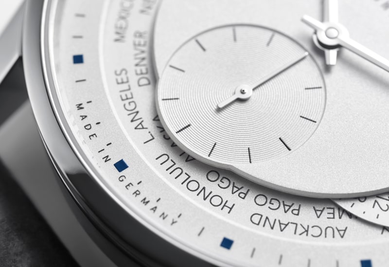 Juwelier-Wagner-Madler-Uhren-Nomos-Glashuette-Zuerich-Kollektion-Ansicht-2 Nahaufnahme eines metallischen, modernen Armbanduhren-Zifferblatts aus der Nomos Zürich Kollektion, das Städtenamen wie Los Angeles, Honolulu und Auckland zeigt. Das Design ist schlicht und elegant, mit einer silberfarbenen Textur und minimalistischer Ästhetik.