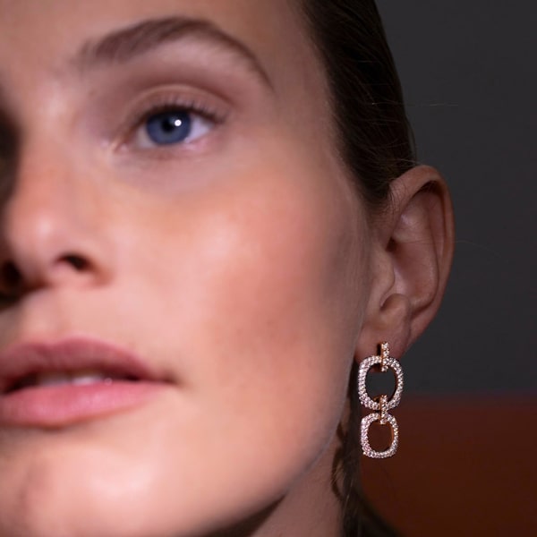 Nahaufnahme einer Person, die funkelnde, geometrisch geformte Bigli-Ohrringe bei sanfter Beleuchtung trägt. Der Fokus liegt auf dem Schmuck, wobei ein unscharfer Hintergrund die Eleganz der Ohrringe und den sanften Ausdruck der Person hervorhebt.