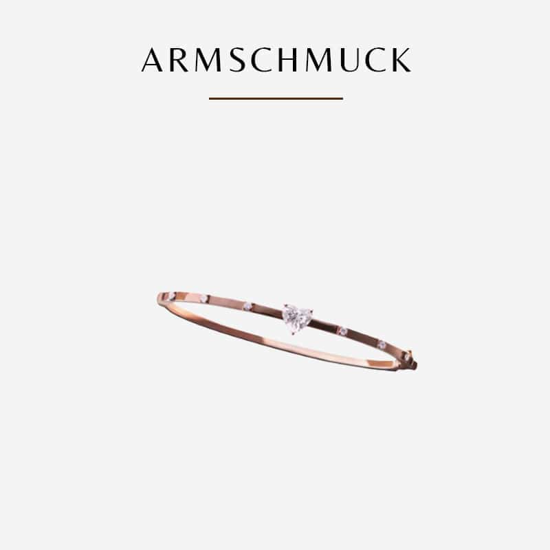 Ein zartes goldenes Armreifarmband mit einem kleinen zentralen Edelstein aus der Diavon-Kollektion steht auf einem schlichten weißen Hintergrund. Über dem Armband steht in eleganter schwarzer Schrift das Wort „Armschmuck“.