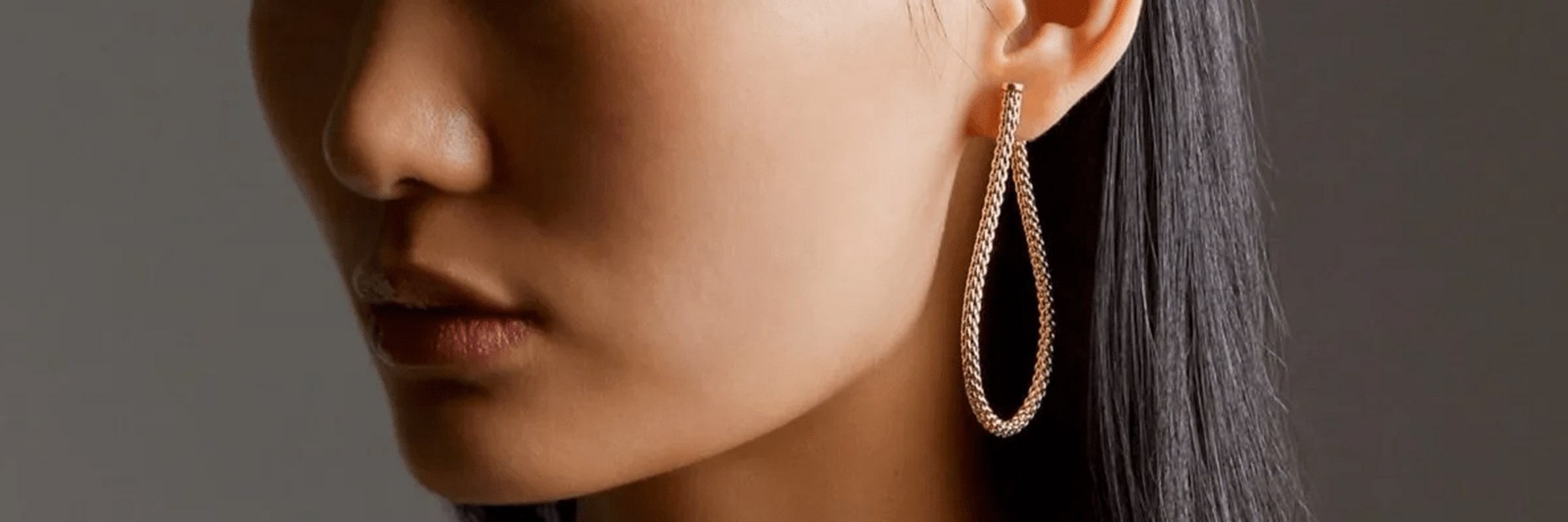 Nahaufnahme einer Person mit glattem, dunklem Haar, die an einem Ohr einen großen, eleganten, tropfenförmigen Ohrring trägt. Der Ohrring scheint mit kleinen funkelnden Steinen verziert zu sein, was ihm ein luxuriöses Aussehen verleiht. Der Hintergrund ist neutral, was den Fokus auf den Ohrring verstärkt.