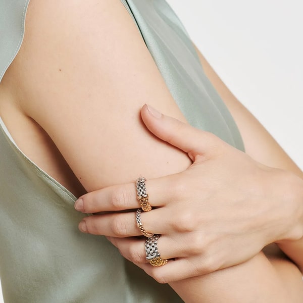 FOPE © 2024 Nahaufnahme einer Person, die drei Ringe, zwei silberne und einen goldenen Fope-Ring, an ihren verschränkten Fingern trägt. Die Person trägt ein hellgrünes, ärmelloses Oberteil und ihre Arme sind locker verschränkt, was eine minimalistische und elegante Ästhetik erzeugt.