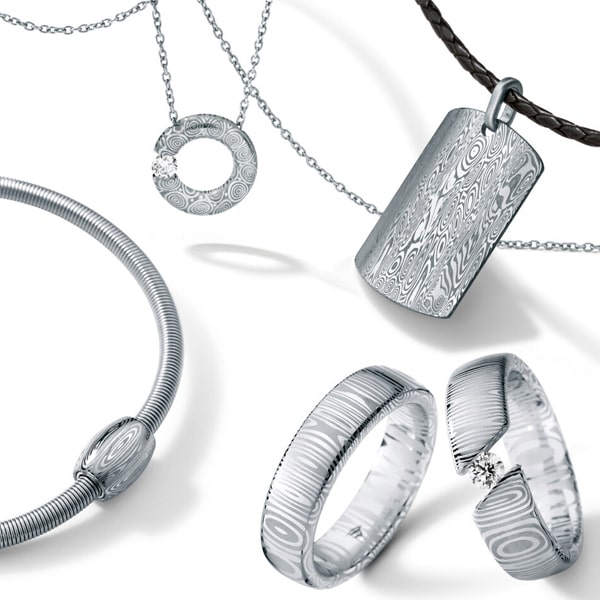 Humphrey © 2024 Ausgestellt wird eine Sammlung von Silberschmuck, darunter zwei Ringe mit Streifenmuster, ein Perlenarmband, eine Halskette mit rundem Anhänger und eine weitere Halskette mit rechteckigem Anhänger an einem Lederband. Jedes Stück ist mit aufwendigen Mustern und kleinen Edelsteinen verziert.