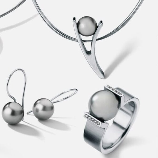 Ein Set modernen Silberschmucks von Humphrey zeigt eine graue Perle. Das Set umfasst eine Halskette mit einem minimalistischen U-förmigen Anhänger, einen passenden Ring mit einem grauen Perlenmittelteil und kleinen eingelegten Edelsteinen sowie elegante Tropfenohrringe mit jeweils einer einzelnen grauen Perle.