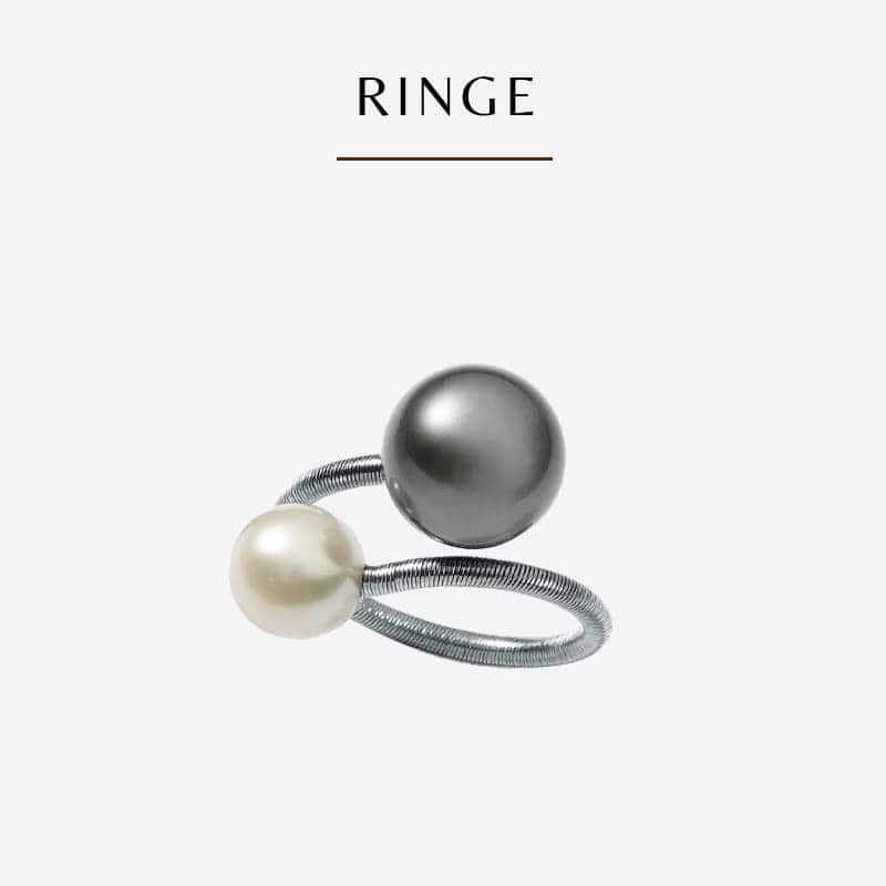 Ein silberner Humphrey-Ring mit zwei kugelförmigen Perlen, einer schwarzen und einer weißen, die an den Enden des offenen Designs des Rings angebracht sind. Das Bild hat eine minimalistische Ästhetik mit dem Wort „RINGE“, das über dem Ring auf weißem Hintergrund geschrieben ist.