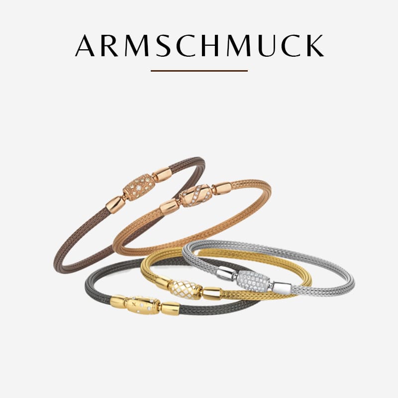 Eine Kollektion aus fünf eleganten Armbändern in verschiedenen Gold-, Braun- und Silbertönen auf weißem Hintergrund. Über den Armbändern steht das deutsche Wort „ARMSCHMUCK“, was darauf hinweist, dass es sich um Armschmuck von Heinz handelt.
