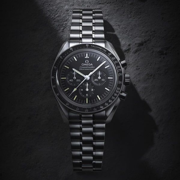 OMEGA © 2025 Eine klassische Omega Speedmaster Chronographenuhr mit Edelstahlgehäuse und -armband ist auf einer strukturierten, felsigen Oberfläche platziert. Die Omega-Uhr verfügt über ein schwarzes Zifferblatt mit drei Hilfszifferblättern und weißen Stundenmarkierungen.