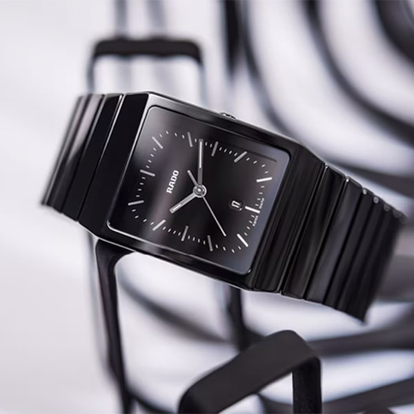 RADO © 2025 Eine elegante, schwarze Luxusarmbanduhr aus der Rado Ceramica Kollektion mit rechteckigem Zifferblatt und minimalistischem Design, auf dem der Markenname „Rado“ zu sehen ist. Der Hintergrund zeigt ein abstraktes schwarz-weißes Muster.