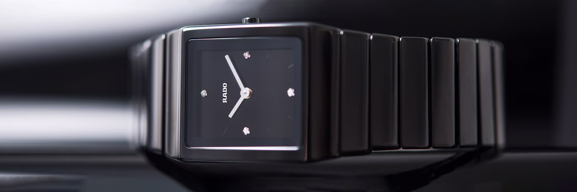 Eine elegante, schwarze, rechteckige Armbanduhr mit einem Metallarmband. Die Uhr verfügt über ein minimalistisches Design mit drei diamantenähnlichen Punkten und schlanken, silbernen Zeigern auf dem Zifferblatt und bietet ein modernes, elegantes Erscheinungsbild.