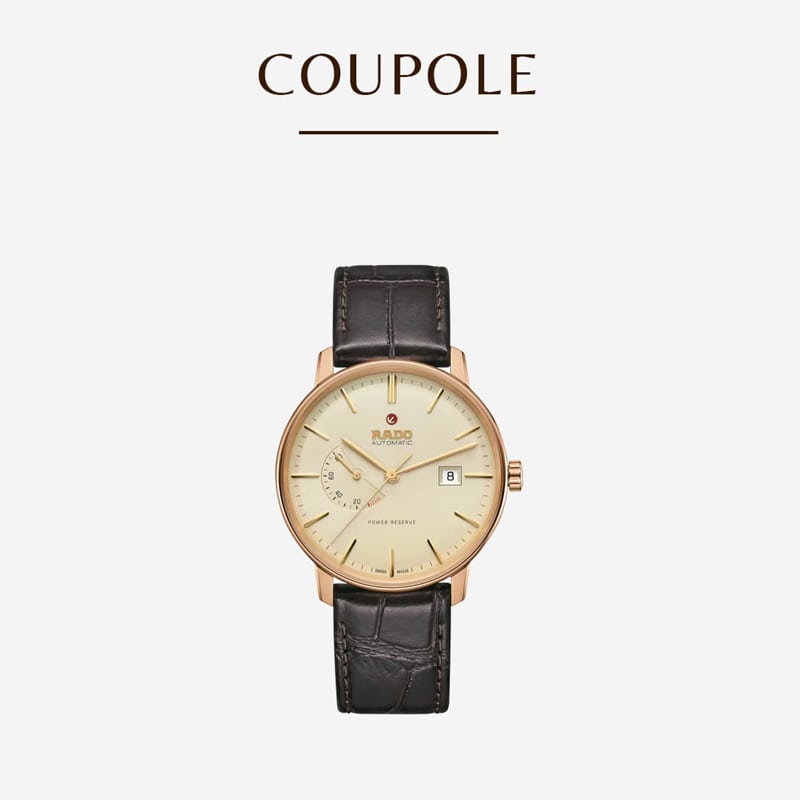 Eine luxuriöse Armbanduhr mit goldenem Gehäuse und weißem Zifferblatt. Sie verfügt über eine Datums- und Gangreserveanzeige und ein braunes Lederarmband. Der Schriftzug „COUPOLE“ steht über der Uhr auf schlichtem weißem Hintergrund.
