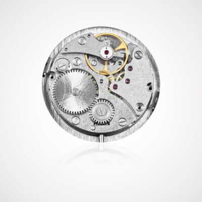 © Juwelier Wagner-Madler Eine Nahaufnahme eines mechanischen Uhrwerks mit komplizierten Metallzahnrädern, Schrauben und kleinen Komponenten vor einem weißen Hintergrund. Die Anordnung der Zahnräder und winzigen Details sind sichtbar und heben die im Uhrenlexikon gepriesene Präzisionstechnik hervor.