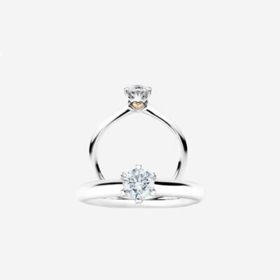 Ein funkelnder Solitär-Diamant-Verlobungsring mit einem eleganten Band aus Weißgold. Der Diamant wird von vier Zinken gehalten und ist elegant auf einem schmalen Band zu sehen. Dieses Schmucklexikon-Juwel verfügt über eine minimalistische Fassung, die die Brillanz des Edelsteins vor einem schlichten, hellen Hintergrund hervorhebt.