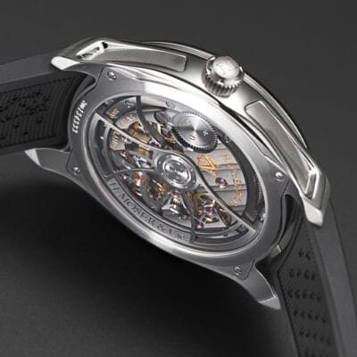 © Juwelier Wagner-Madler e.K. Eine Nahaufnahme einer Luxusuhr mit transparentem Gehäuseboden, der die komplizierten inneren Mechanismen offenbart. Die metallischen Komponenten, Zahnräder und Inschriften sind sichtbar und zeigen die im Uhrenlexikon beschriebene Handwerkskunst. Die Uhr hat ein schwarzes Armband mit strukturierter Oberfläche.