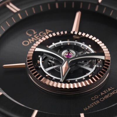 OMEGA © 2024 Nahaufnahme eines Omega-Uhrenzifferblatts, in dessen Mitte der aufwendig gestaltete Tourbillon-Mechanismus zu sehen ist. Das Zifferblatt weist Akzente aus Roségold auf, das Omega-Logo und der Text „Co-Axial Master Chronometer“ sind sichtbar und betonen den Luxus und die Präzision der Uhr, die im Uhrenlexikon Anerkennung finden.