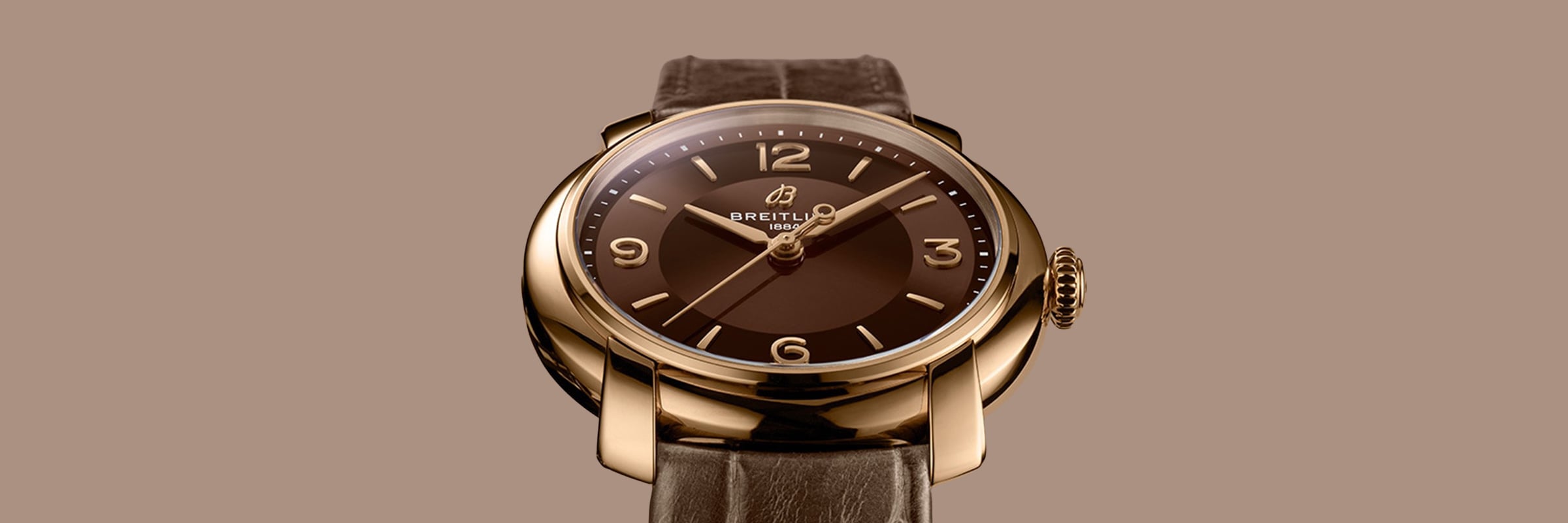 Eine luxuriöse Breitling Lady Premier Armbanduhr mit braunem Zifferblatt, goldenem Gehäuse und braunem Lederarmband, das vor einem passenden braunen Hintergrund angezeigt wird. Die Uhr zeigt stilvoll die Zeit als 10:10 an.