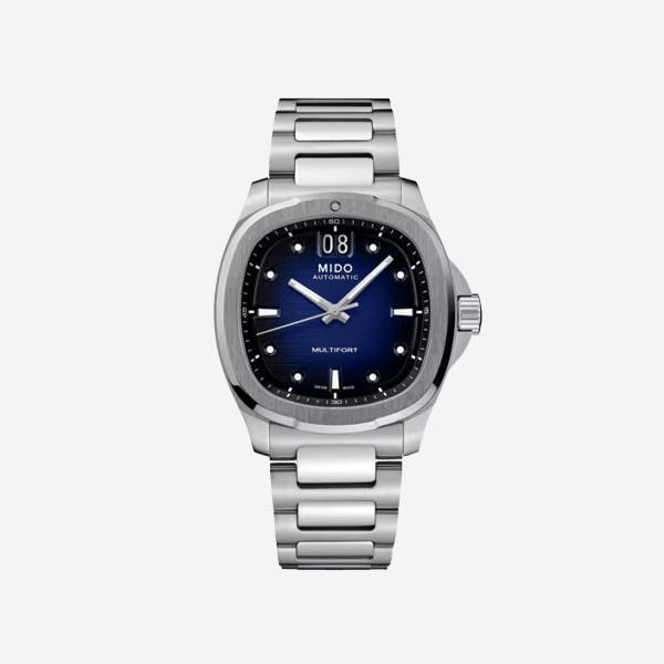 Eine Mido Multifort Automatikuhr aus Edelstahl mit blauem Zifferblatt, silbernen Indexen, silbernen Zeigern und einem Datumsfenster auf der 12-Uhr-Position auf weißem Hintergrund.