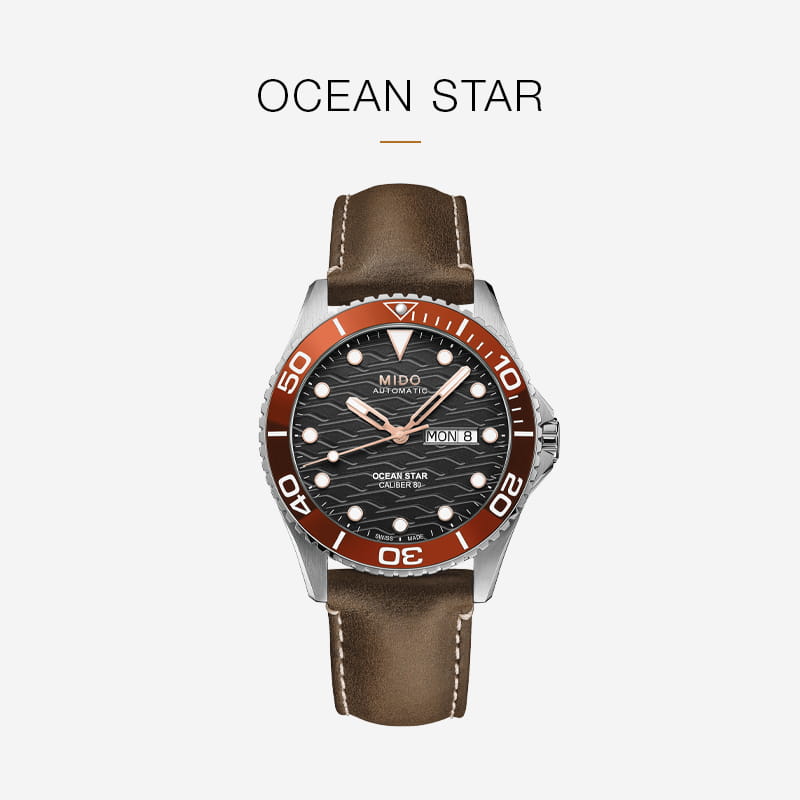 Eine Mido Ocean Star Armbanduhr mit einem braunen Lederarmband, einer roten Lünette und einem gewellten schwarzen Zifferblatt, das den Tag und das Datum anzeigt, zentriert auf einem weißen Hintergrund mit dem Text "Mido OCEAN STAR" darüber.