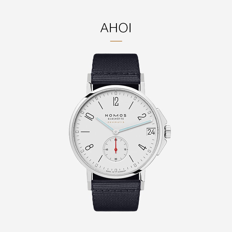 Eine silberne NOMOS Glashütte Ahoi-Armbanduhr mit weißem Zifferblatt, schwarzen Ziffern, Datumsfenster und kleiner roter Sekundenanzeige an einem dunklen Stoffarmband auf weißem Grund.
