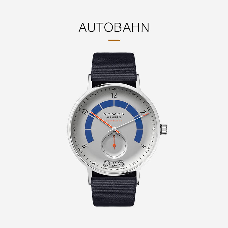 Eine silberne NOMOS-Glashütte-Autobahn-Armbanduhr mit blauem Bogen auf dem Zifferblatt, Datumsfenster bei 6 Uhr und schwarzem Stoffarmband steht auf weißem Grund, hervorgehoben durch den Schriftzug Autobahn" darüber.