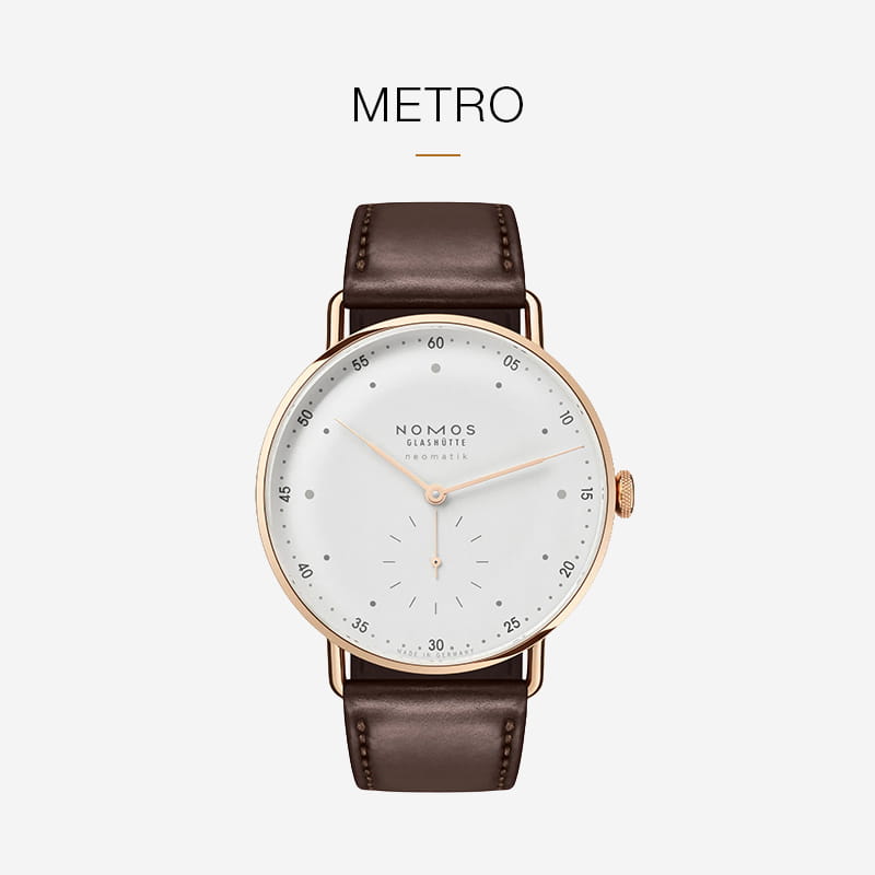 Eine NOMOS Glashütte Metro-Armbanduhr mit weißem Zifferblatt, goldenem Gehäuse und minimalistischem Design passt perfekt zu einem dunkelbraunen Lederarmband, das die raffinierte Handwerkskunst von NOMOS Glashütte vor einem hellen Hintergrund zeigt.