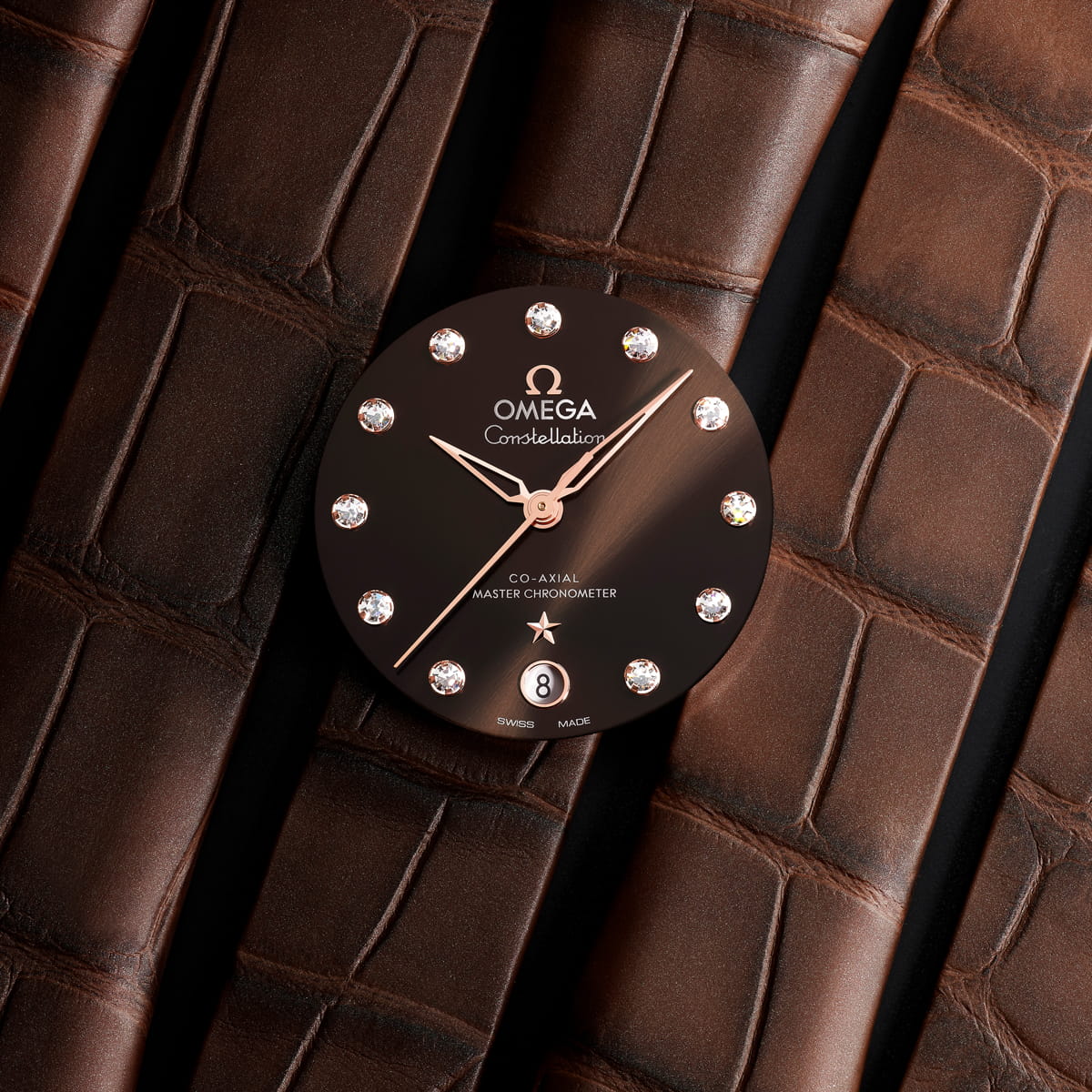 Eine Nahaufnahme des Zifferblatts einer OMEGA Constellation mit diamantbesetzten Indexen, roségoldenen Zeigern und einem Datumsfenster bei 6 Uhr vor einem Hintergrund aus dunkelbraunem, strukturiertem Leder.