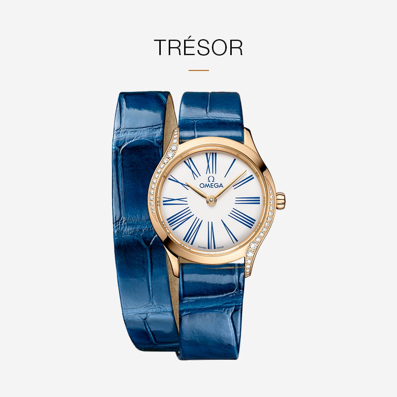 Eine goldene OMEGA DeVille Trésor Uhr mit weißem Zifferblatt, blauen römischen Ziffern, Diamantakzenten auf dem Gehäuse und einem glänzenden blauen Lederarmband mit doppelter Umschlingung, dargestellt auf einem hellen Hintergrund.