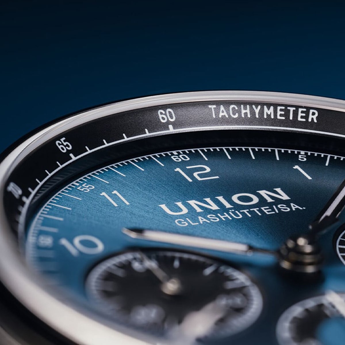 Nahaufnahme einer luxuriösen Union Glashütte-Armbanduhr mit blauem Zifferblatt, detaillierten Stundenmarkierungen, Chronographenzifferblättern und der Aufschrift "UNION GLASHÜTTE/SA". Der äußere Ring ist mit einer Tachymeterskala versehen.