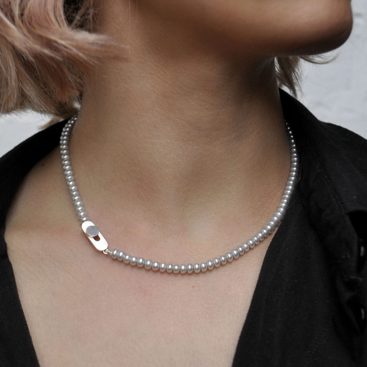 Eine Person, die eine kurze Perlenkette mit einer silbernen Getränkedosenlasche als Anhänger trägt, gepaart mit einem schwarzen Kragenhemd. Das Foto konzentriert sich auf den Hals- und Schlüsselbeinbereich und hebt den einzigartigen DOPPELLUDWIG-Accessoire-Stil hervor.