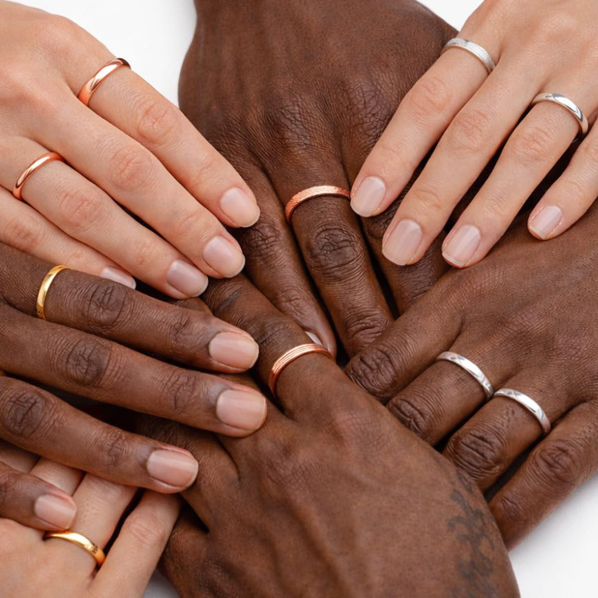 DOPPELLUDWIG © 2026 Mehrere Hände in verschiedenen Hauttönen, die jeweils schlichte DOPPELLUDWIG Ringe in Gold, Roségold und Silber tragen, sind in einem kreisförmigen Muster auf weißem Hintergrund angeordnet.