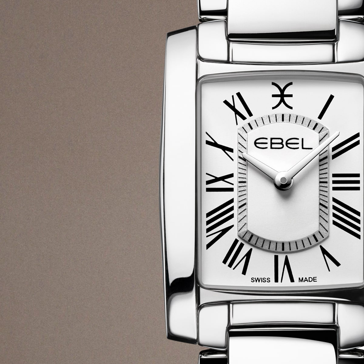 EBEL © 2026 Nahaufnahme einer silbernen Ebel-Armbanduhr mit rechteckigem Zifferblatt, schwarzen römischen Ziffern und silbernen Zeigern vor einem schlichten braunen Hintergrund. Das Ebel-Logo und "SWISS MADE" sind auf dem Zifferblatt sichtbar.