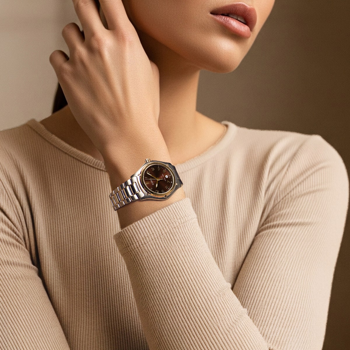 Eine Frau in einem beigefarbenen langärmeligen Oberteil posiert mit der linken Hand im Nacken und trägt eine elegante silberne Armbanduhr Ebel 1911 mit dunklem Zifferblatt und goldenen Akzenten am Handgelenk. Ihre Lippen und ihr Kinn sind zu sehen.