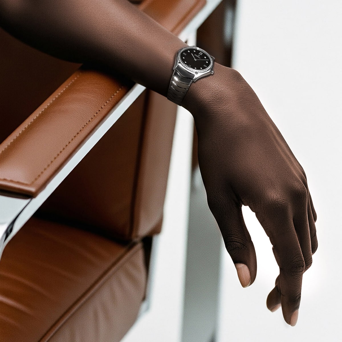 Eine Person mit dunkler Hautfarbe stützt ihre Hand auf die Armlehne eines braunen Ledersessels und präsentiert eine elegante silberne Ebel 1911-Armbanduhr mit schwarzem Zifferblatt.