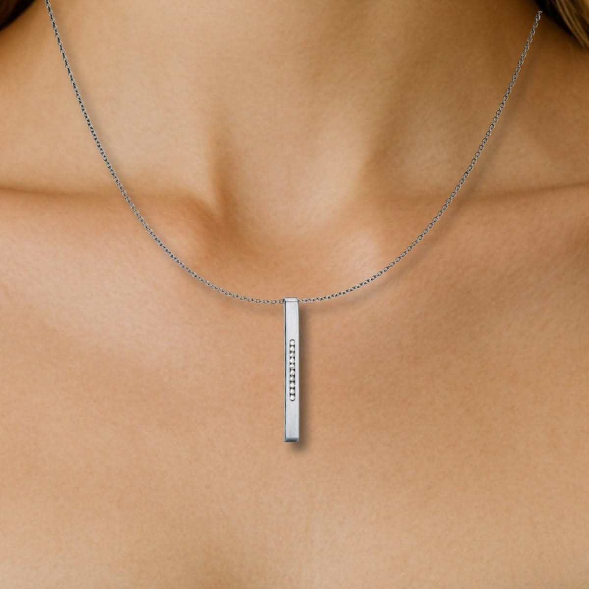 Nahaufnahme des Halses einer Person, die eine zarte Humphrey-Kette mit einem vertikalen rechteckigen Anhänger trägt, der in der Mitte eine Reihe kleiner, funkelnder Steine aufweist.
