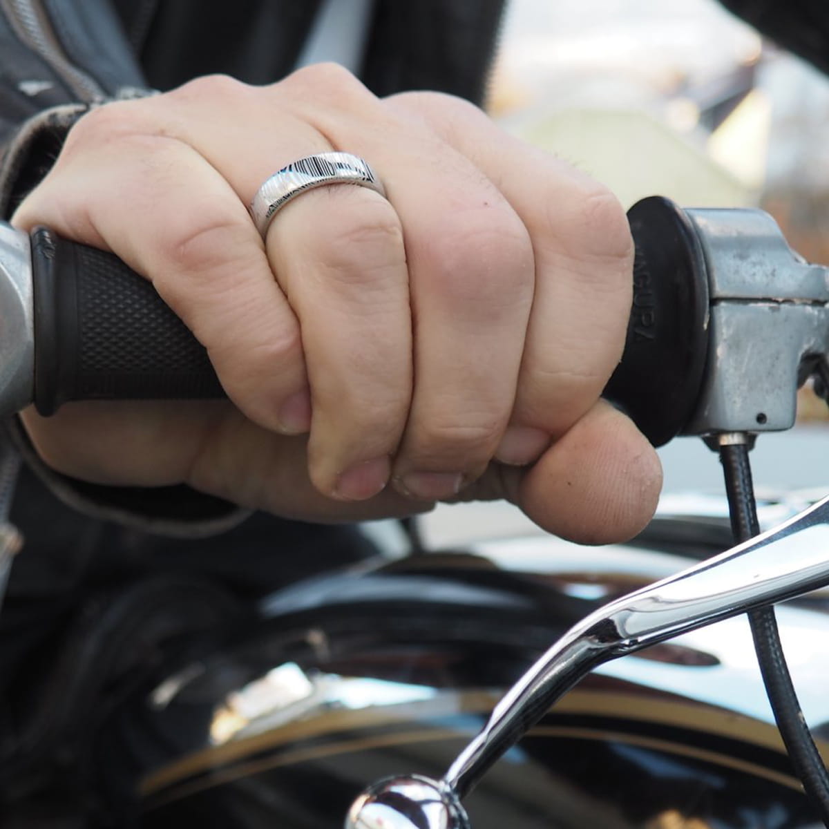 Eine Nahaufnahme von Humphreys Hand, die den Lenker eines Motorrads umgreift. Er trägt einen silbernen Ring am Mittelfinger, und der Gashebel und der Spiegel des Motorrads sind zu sehen.
