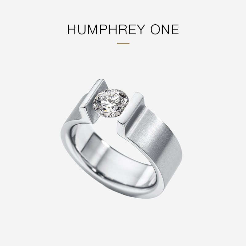 Moderner Silberring von Humphrey mit breitem Band und offener Fassung, in der ein einzelner runder Diamant zwischen zwei vertikalen Zacken gefasst ist. Text oben liest "HUMPHREY ONE" auf einem hellen Hintergrund.
