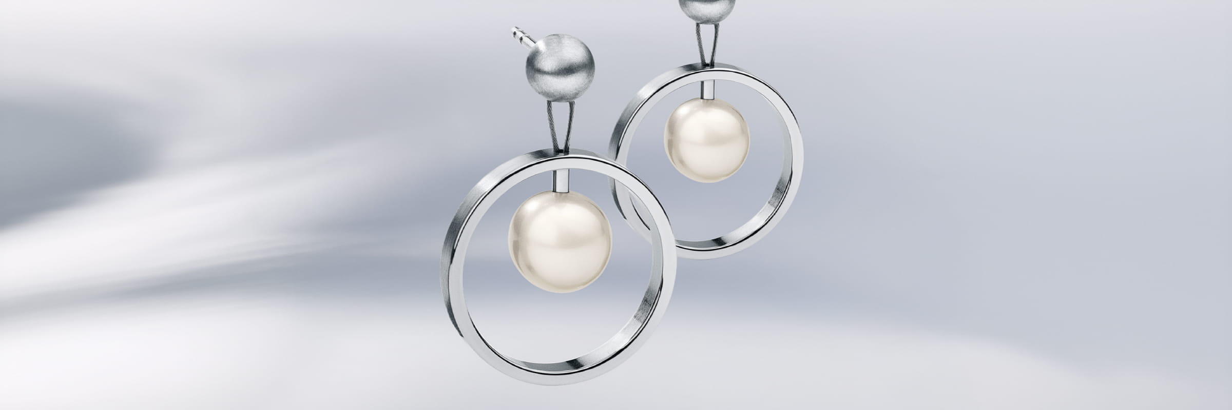 Ein Paar moderne silberne Humphrey Ohrschmuck-Ohrringe mit kreisförmigen Reifen und baumelnden weißen Perlen, die vor einem weichen, verschwommenen Lichthintergrund gezeigt werden.