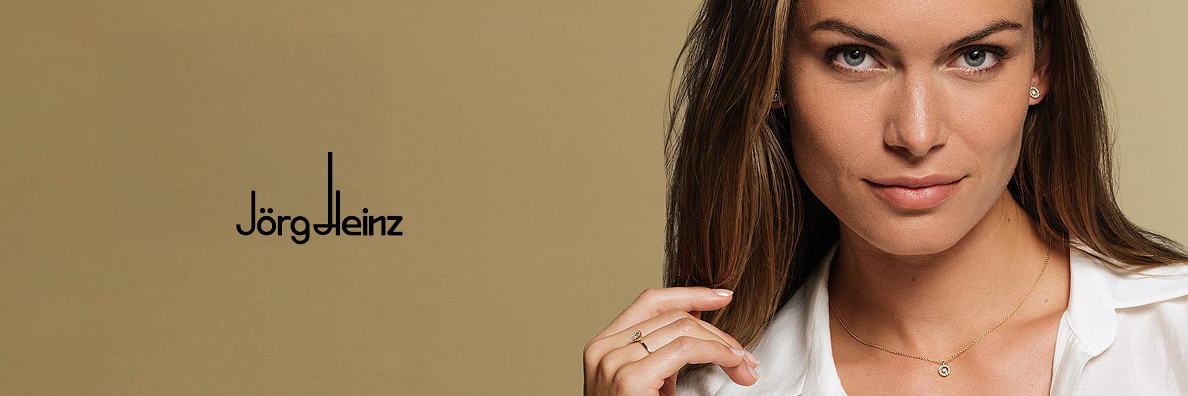 Eine Frau mit langen braunen Haaren und weißer Bluse trägt dezenten Jörg Heinz-Schmuck: eine goldene Halskette mit einem kleinen Anhänger, passende Ohrstecker und Ringe. Auf dem beigen Hintergrund ist links das Jörg Heinz-Logo zu sehen.